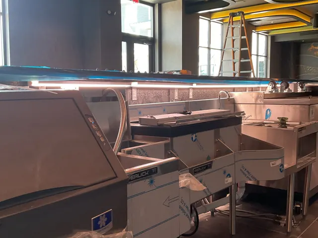 Bar line with an ice machine and beverage stations still covered in protective film, with an under-counter LED strip light