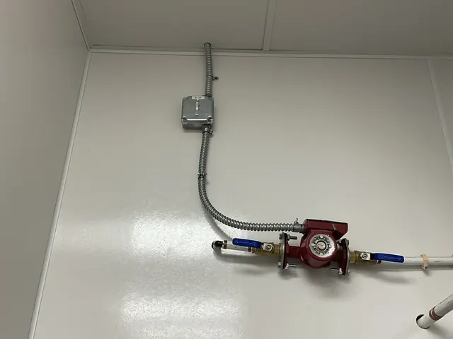 Red circulator pump with blue-handled valves on a wall, connected to a switch box above it