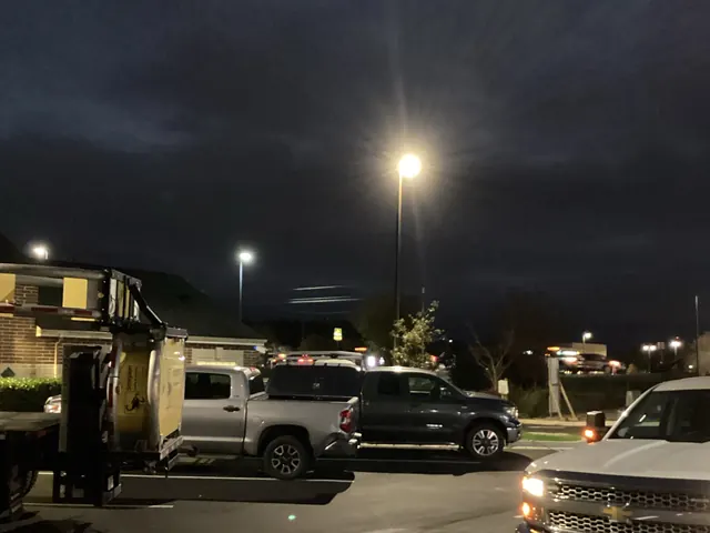 Night view of a parking lot lit by tall pole lights, with several pickup trucks parked in the foreground
