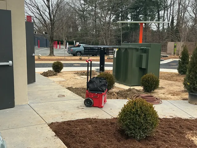 Green pad-mounted transformer on a concrete pad in a landscaped area beside a sidewalk