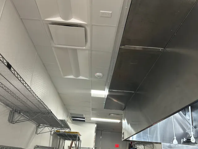 Commercial kitchen ceiling with two lit recessed LED fixtures beside a stainless steel exhaust hood