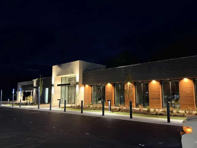 Night view of a lit commercial bank building entrance with wood-panel facade, bollard lights and pole lights