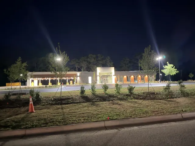 Wide night view of a commercial bank building with a lit drive-thru canopy, parking-lot pole lights and landscape lighting